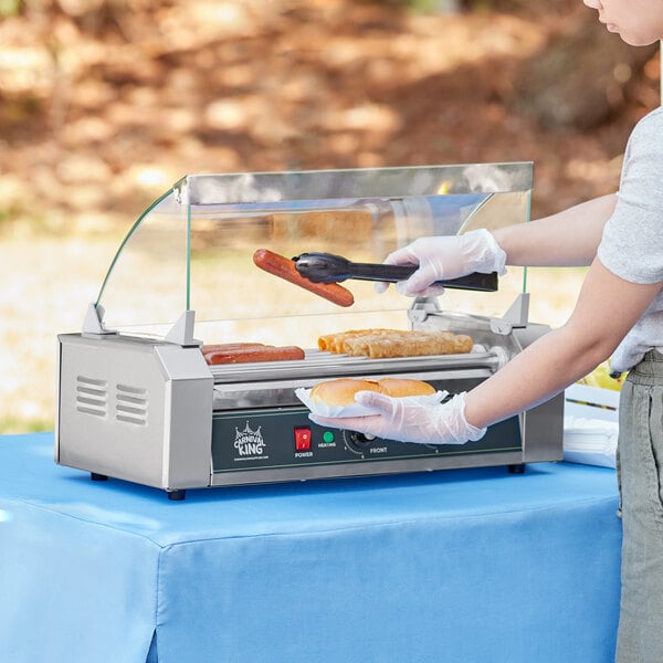 A woman using a Carnival King hot dog roller to cook hot dogs on a counter.