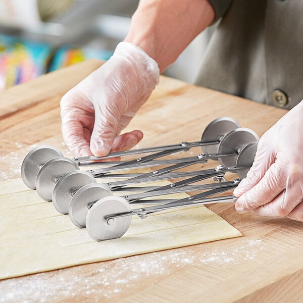 A person in gloves using a Choice stainless steel pastry cutter wheel to cut dough.
