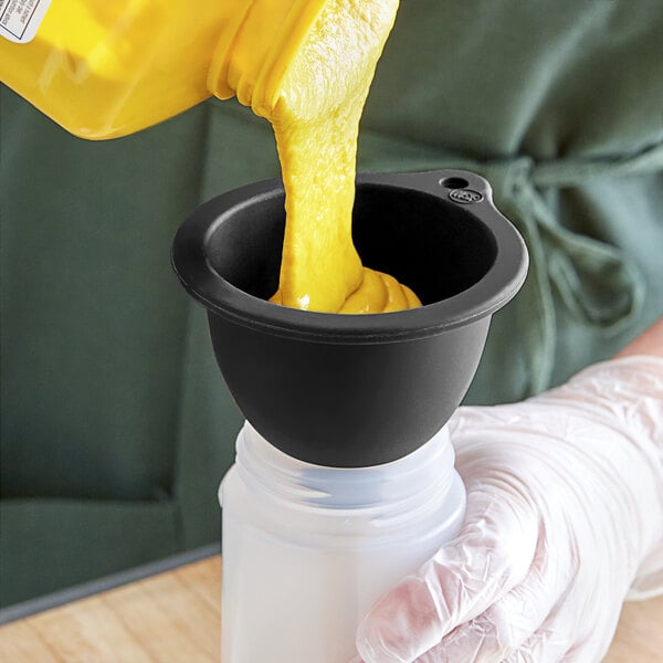 A person using a Tablecraft black silicone funnel to pour yellow liquid into a plastic container.