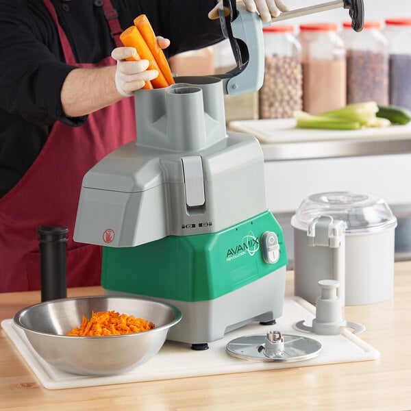 A person in an apron using an AvaMix food processor to shred carrots.