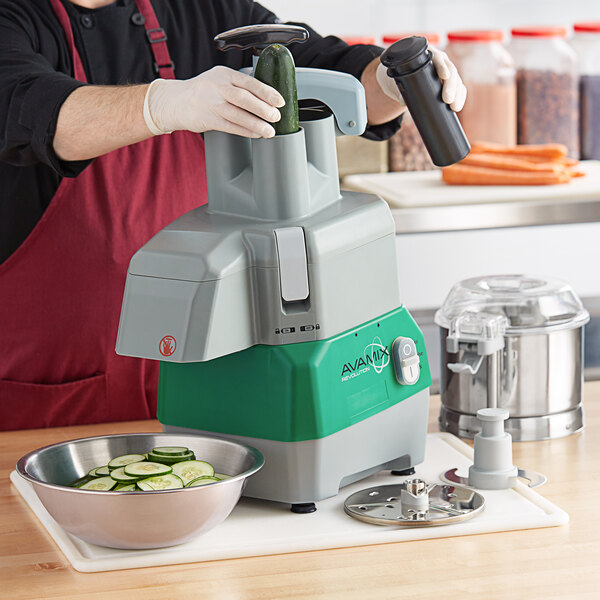 A person in a red apron using the AvaMix Revolution food processor to slice cucumbers.