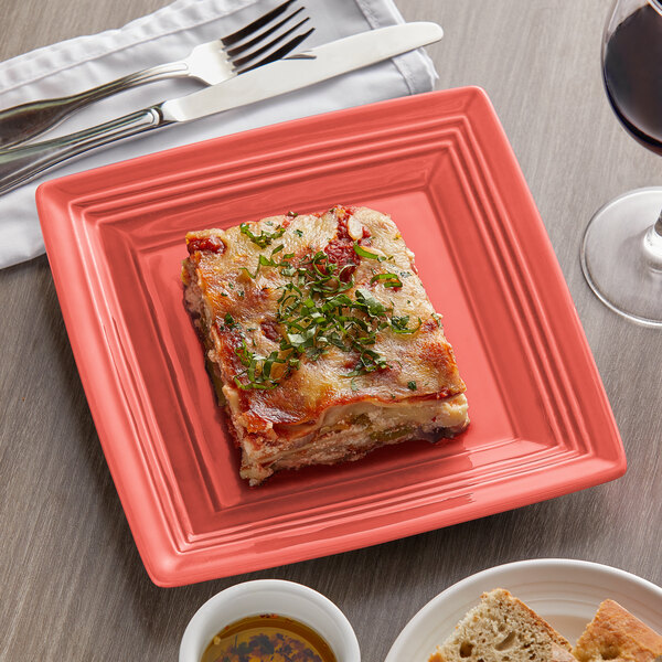 A Tuxton Concentrix square china plate with lasagna and wine on a table.
