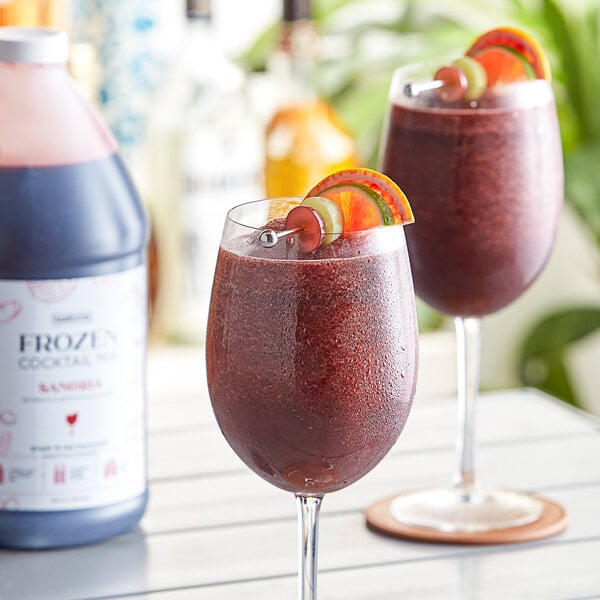 A bottle of Narvon Sangria Frozen Cocktail Mix with two wine glasses filled with sangria, one garnished with fruit.