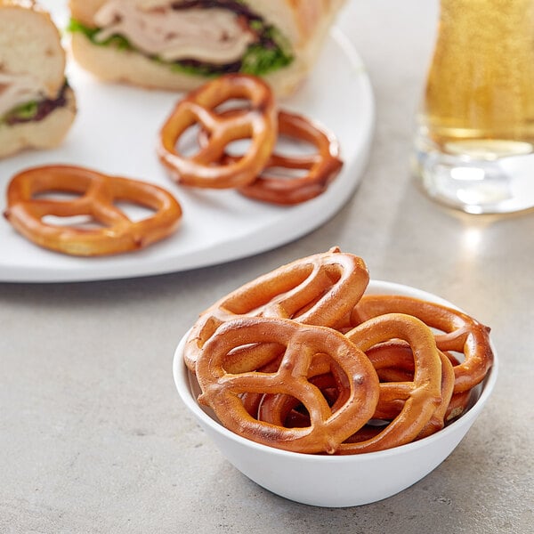 A bowl of Tom Sturgis Low Sodium Specials pretzels on a table with a sandwich.