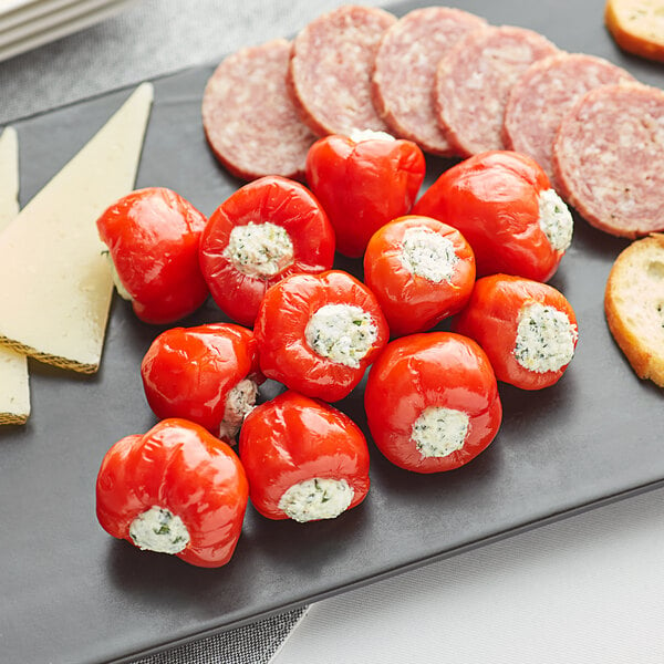 A plate with cheese, crackers, Peppadew sweet piquante peppers, salami, and sausage on a table.