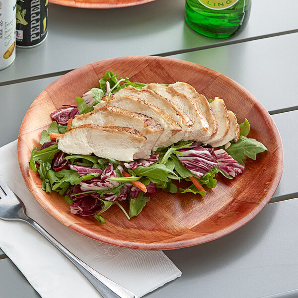 A Choice woven wood plate with chicken and salad on a table
