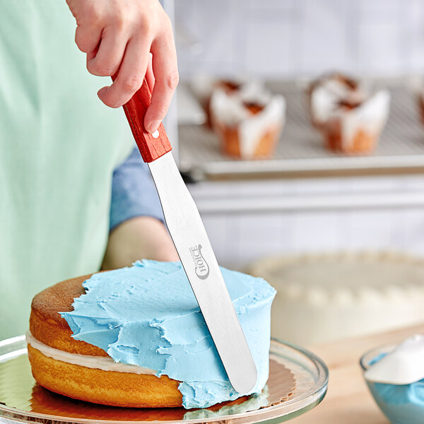 A person using a Choice straight baking spatula with a wood handle to frost a white cake.