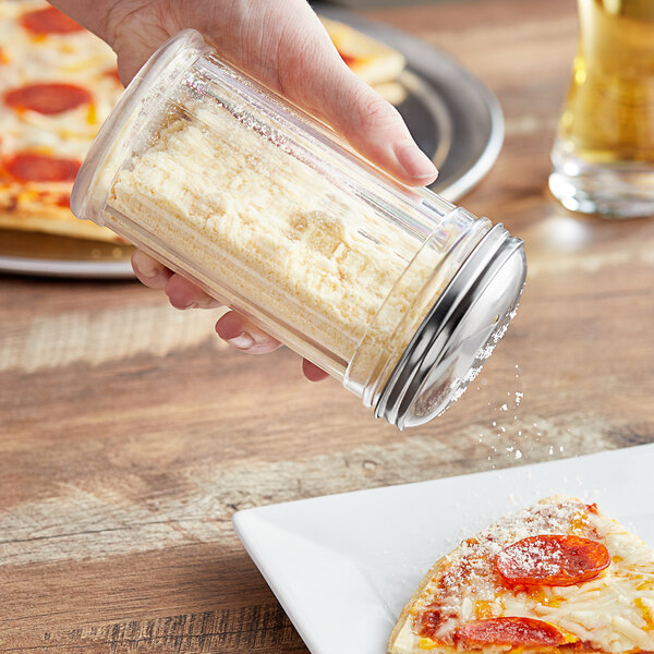 A person using a Choice plastic cheese shaker to sprinkle cheese on a slice of pizza.