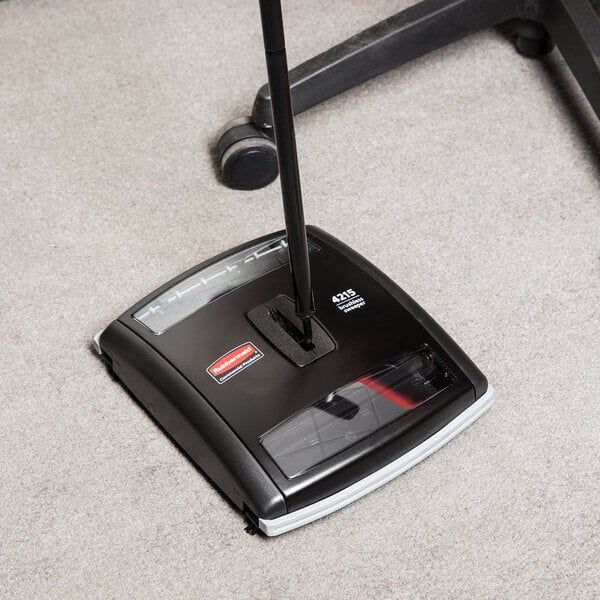 A black Rubbermaid Executive Series floor sweeper on the floor.