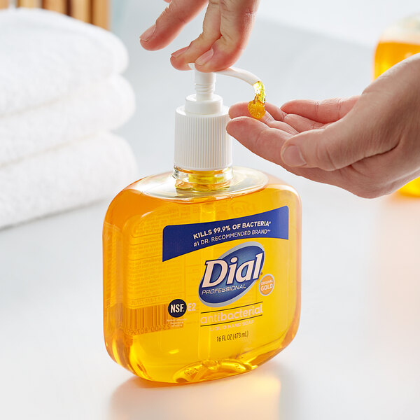 A hand pouring Dial Professional Gold Antibacterial Liquid Hand Soap into another bottle.