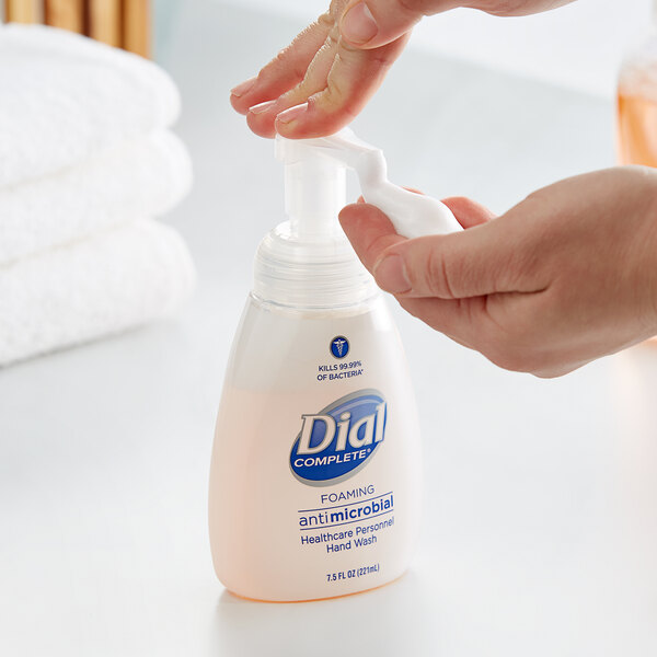 A person holding a plastic bottle of Dial foaming hand wash.