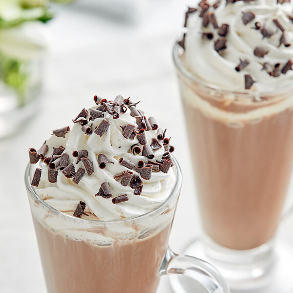 A glass cup of chocolate milkshake with whipped cream and chocolate shavings.