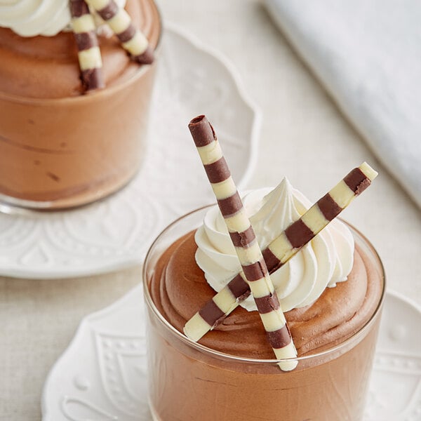 Two chocolate desserts with whipped cream and chocolate drizzle in glasses.