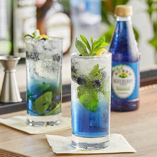 Two glasses of Rose's Blueberry Syrup cocktails with blue liquid and mint leaves on a table.