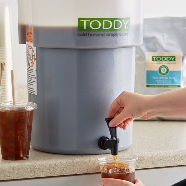 A person pouring Toddy New Orleans style cold brew coffee into a plastic cup.
