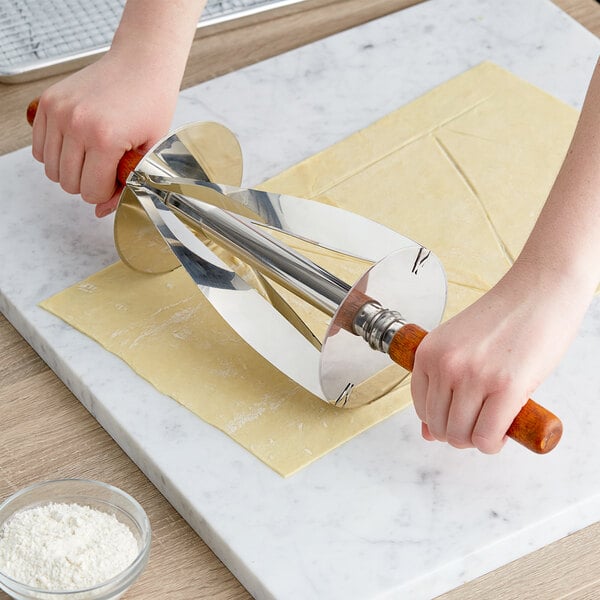 A hand using a Choice stainless steel croissant cutter to cut dough.