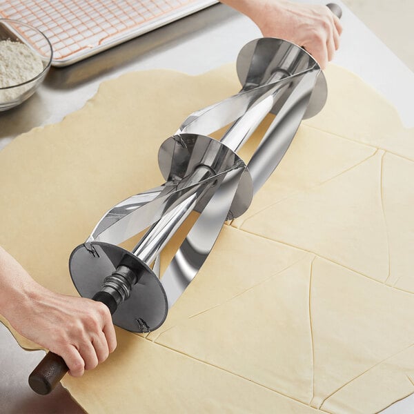 A person rolling dough with a Choice stainless steel croissant cutter.