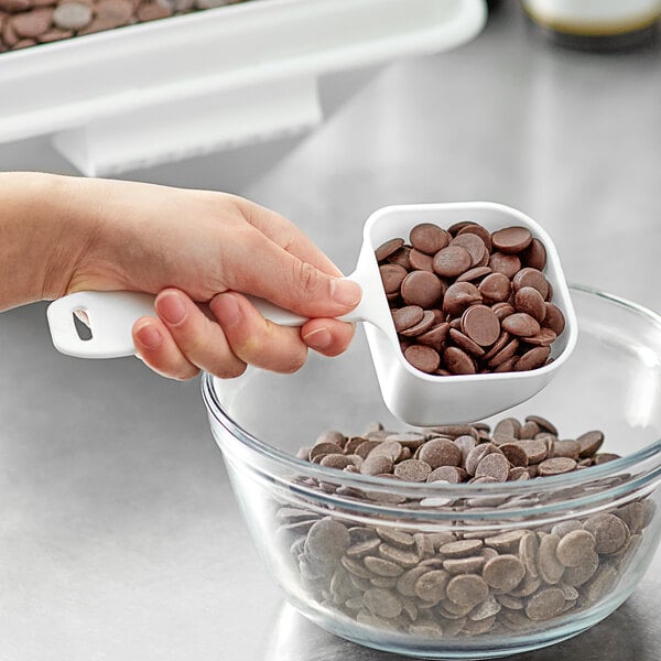 A person using a Baker's Mark white plastic utility scoop to pour chocolate chips into a bowl.