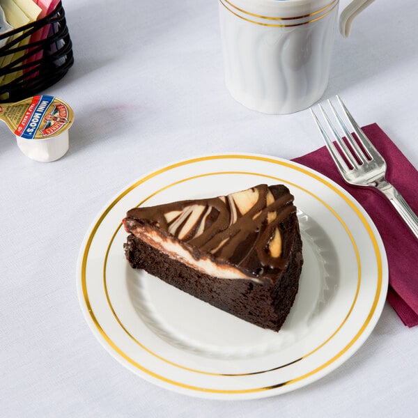 A piece of chocolate cake on a Fineline ivory plastic plate with gold bands next to a cup of coffee.