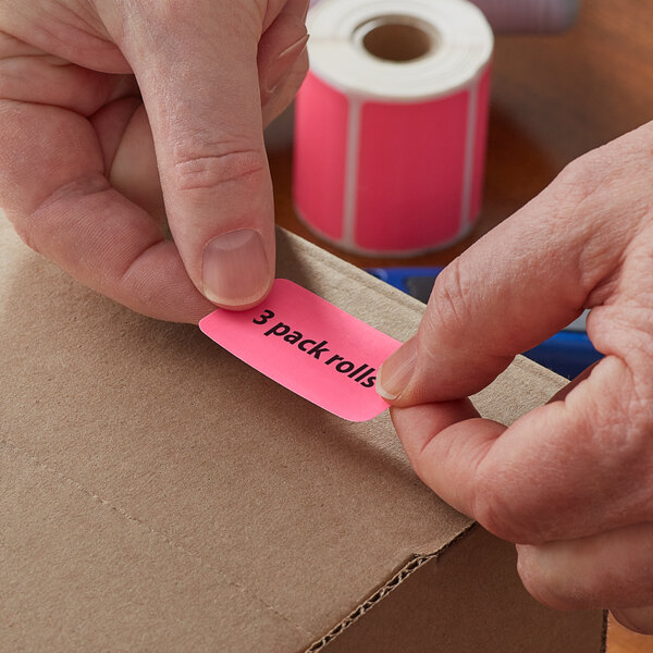 A person's hand using a pink Lavex Direct Thermal label to put a label on a box.