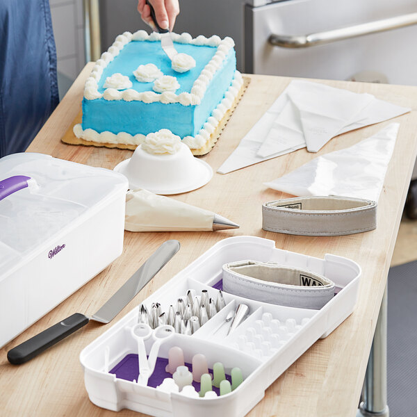 A person using a Wilton cake decorating set to cut a white cake.