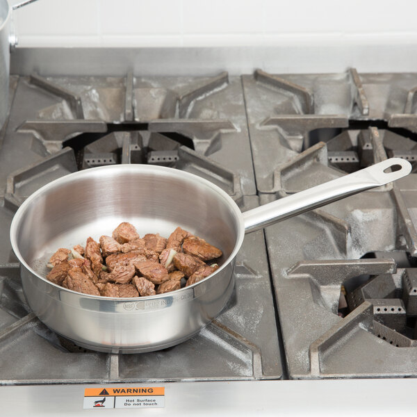 A Vollrath Optio saute pan filled with meat on a stove.