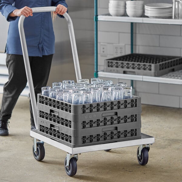 A person pushing a Regency aluminum dish rack dolly with a handle full of glasses.