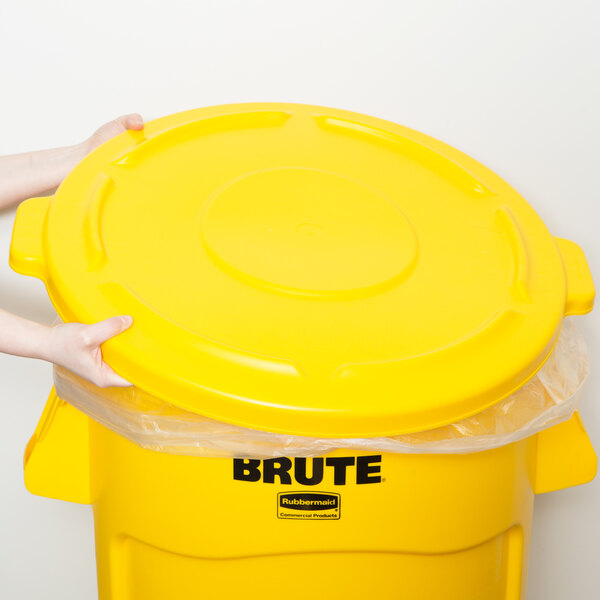 A person holding a yellow Rubbermaid BRUTE trash can with a yellow lid.