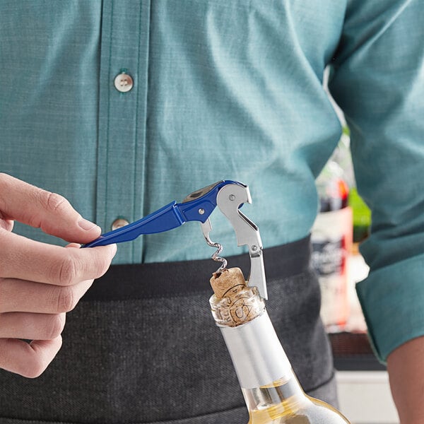 A person using an Acopa waiter's corkscrew with a blue metal handle to open a bottle of wine.