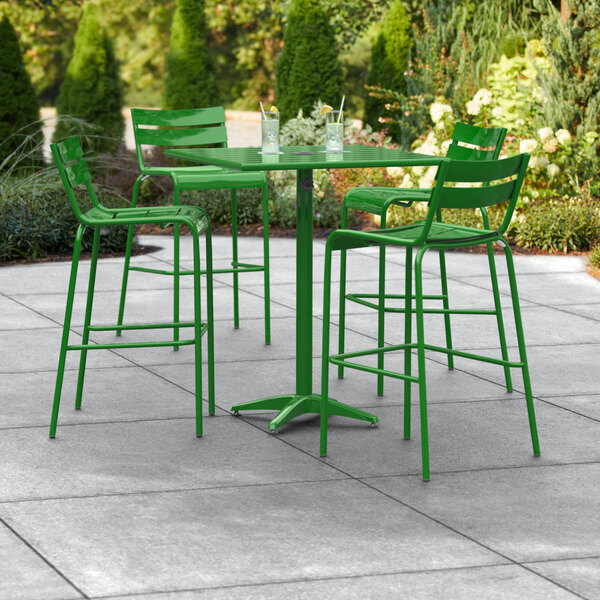 A green Lancaster Table & Seating bar height table and chairs on an outdoor patio.