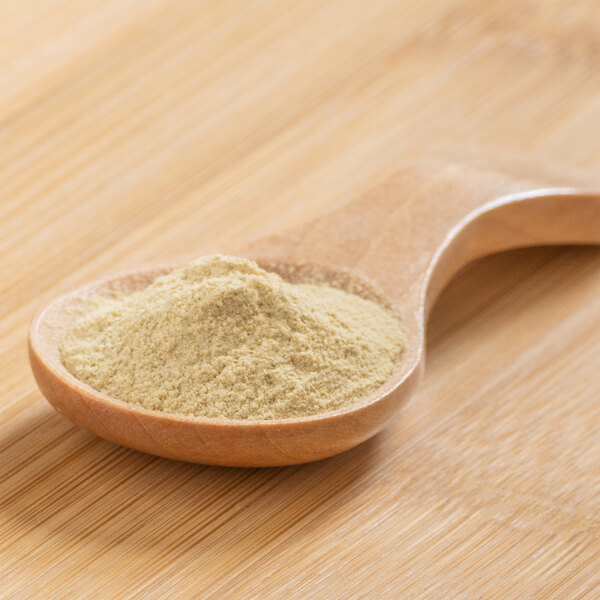 A spoonful of lime peel powder on a wood surface.