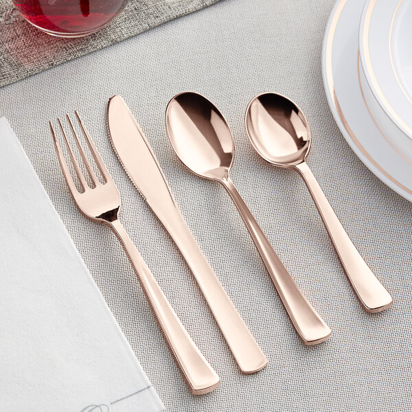 Visions rose gold plastic cutlery set on a table with a spoon and fork.