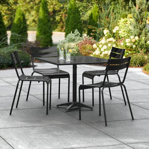A black Lancaster Table & Seating aluminum table with four chairs on an outdoor patio.