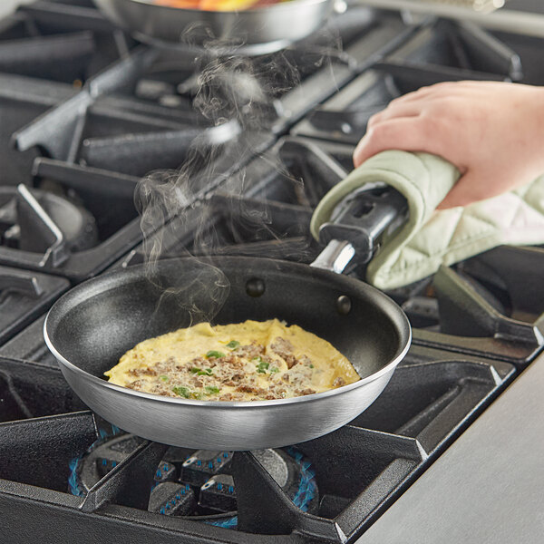 A person using a Vollrath Wear-Ever non-stick fry pan to cook an omelette on a stove.