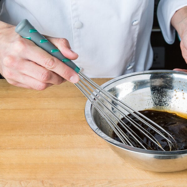 A person using a Vollrath stainless steel whisk to mix brown liquid in a bowl.