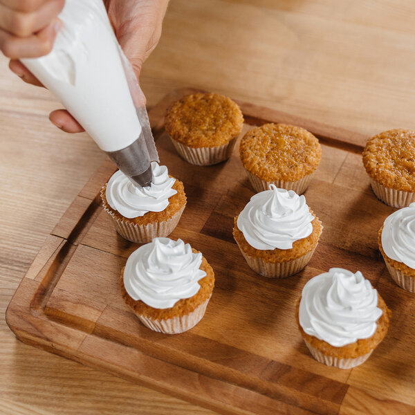 A hand using an Ateco open star piping tip to frost a cupcake with white frosting.