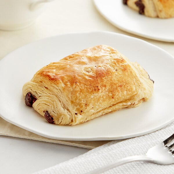 A close-up of a White Toque chocolate croissant on a white plate.