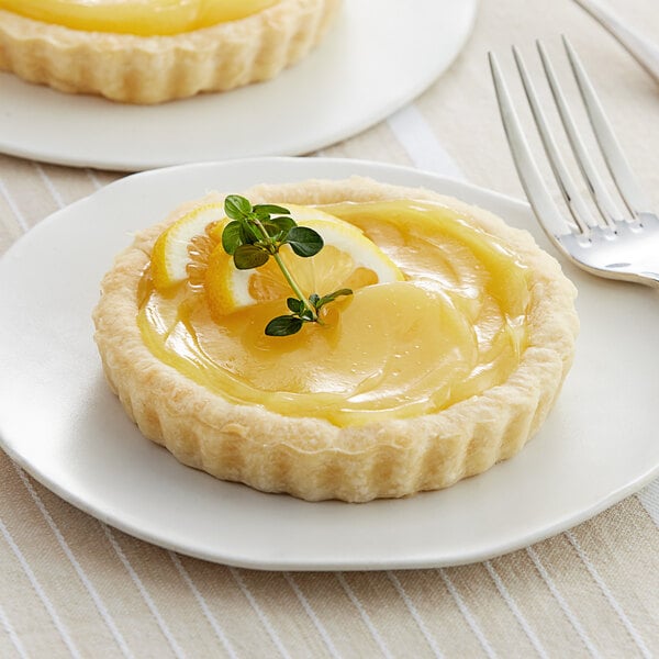 A plate with two lemon curd tarts with lemon slices and a sprig of lemon.