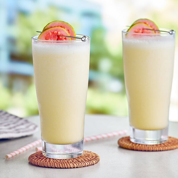 A close up of a glass of Capora Guava Passion Fruit smoothie with fruit on the rim.