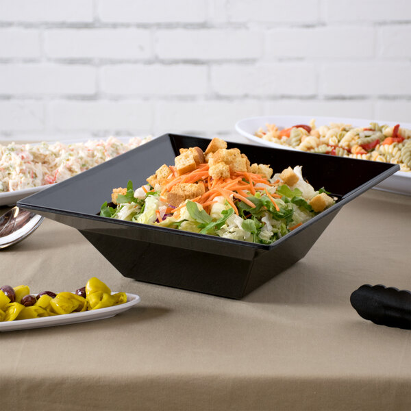 A black Siciliano square bowl filled with salad on a table.