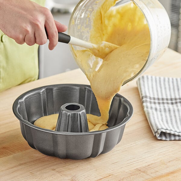 A person pouring yellow cake batter into a Baker's Mark fluted bundt cake pan.