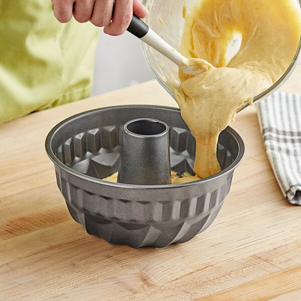 A person pouring cake batter into a black Choice fluted cake pan.