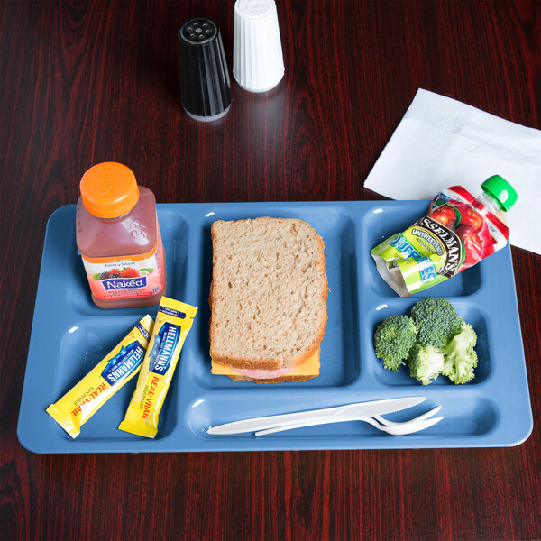 A blue Cambro 6 compartment serving tray with food including a sandwich, a drink, and a fruit.