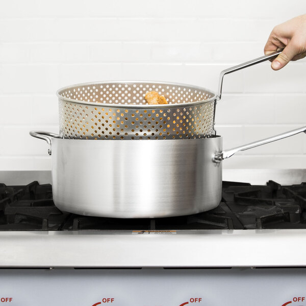 A hand using tongs to hold a Vollrath Wear-Ever fry pot full of food over a stove.