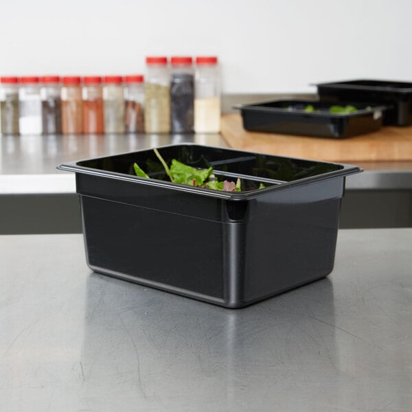 A black Cambro 1/2 size plastic food pan filled with green leafy vegetables on a counter.