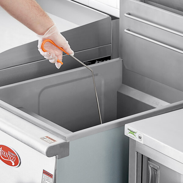 A gloved hand uses an orange coated Fryclone cleaning rod to clean a stainless steel deep fryer.