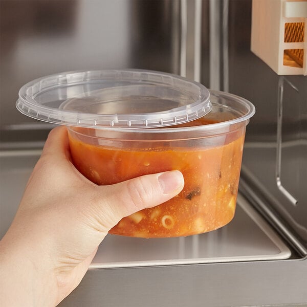 A hand holding a Choice plastic container of soup in front of a microwave.