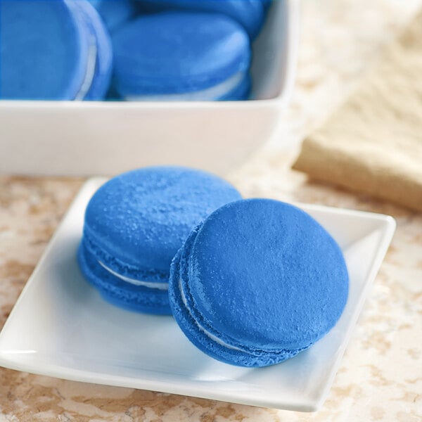 A white plate of blue macaroons with blue cookies on it.
