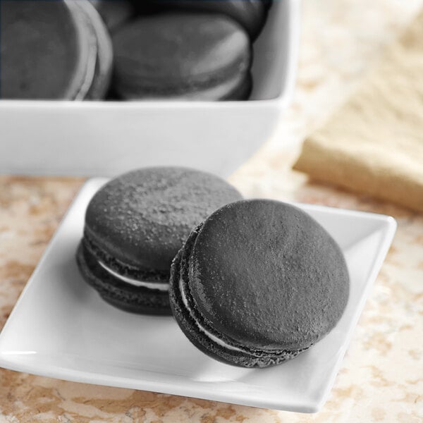 A white plate with black macarons and a white bowl of black food coloring.
