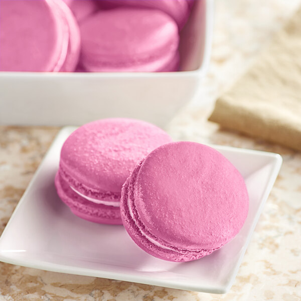 Pink macarons on a white plate with a white bowl.